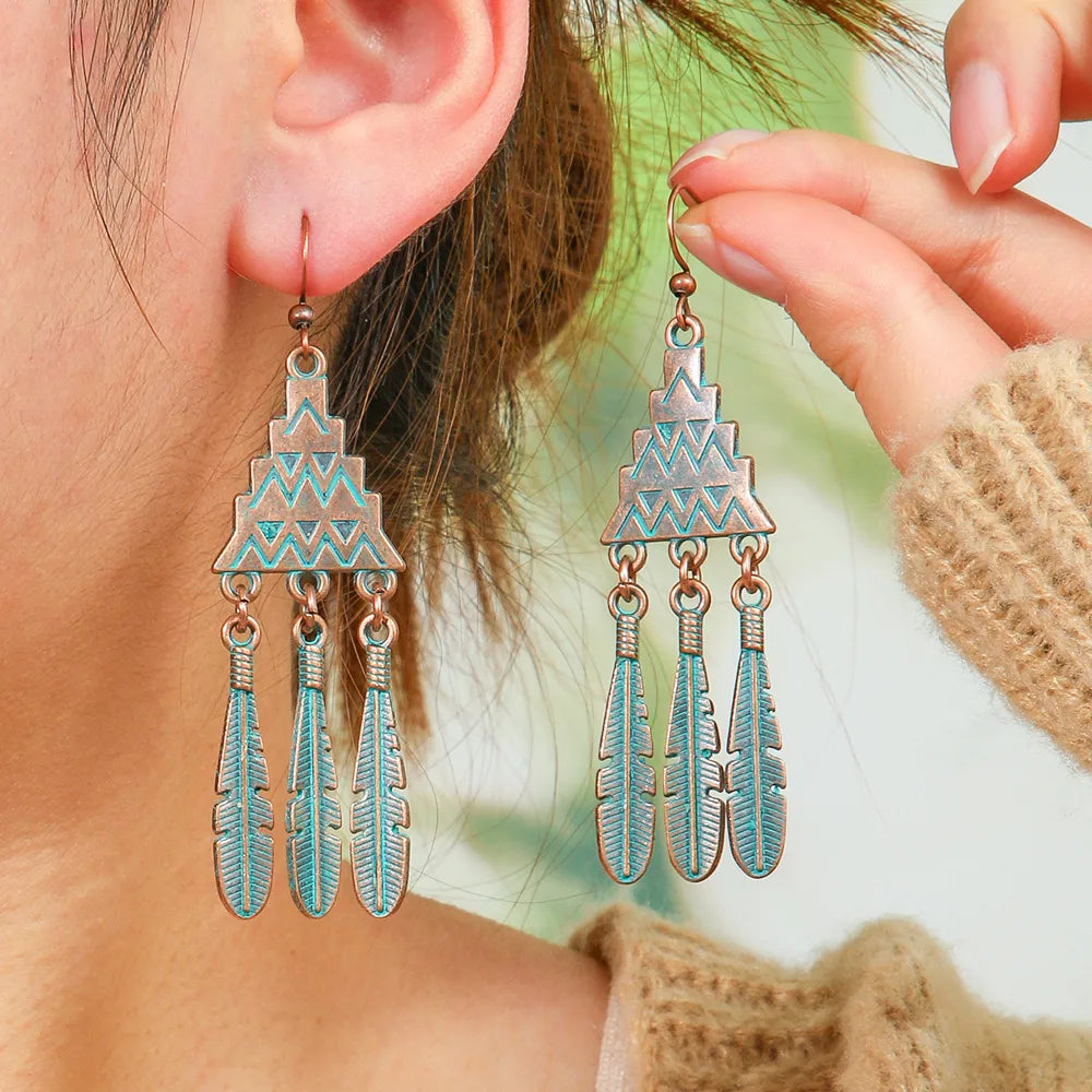 A woman wearing oxidised geometric feather dangle earrings with teal patina, showcasing their bohemian style.