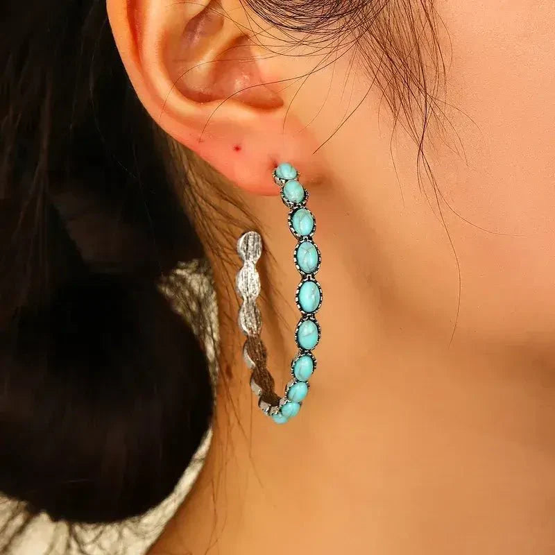 Close-up of the top part of an oxidised silver hoop earring, showing oval turquoise stones and the ear post against a wooden 