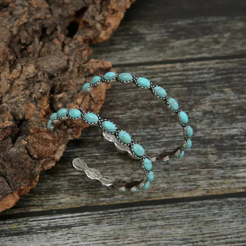 Two large oxidised silver hoops with oval turquoise stones on the front and twisted metal on the back, resting on a textured 