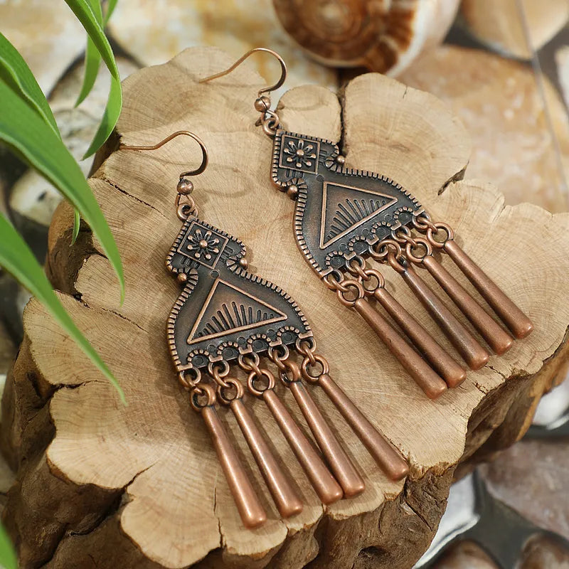 Long oxidised tribal dangle earrings with geometric patterns and tassel drops on wooden backdrop - front view | Earthy Origin