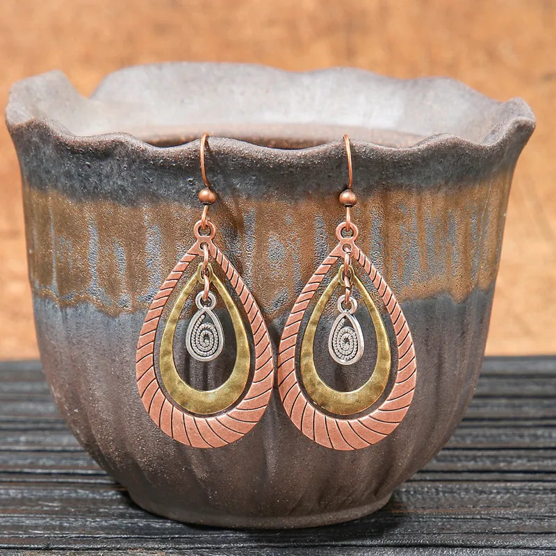 Close-up of oxidised earrings with mixed metal layered teardrops, featuring a spiral charm, resting in a ceramic pot.