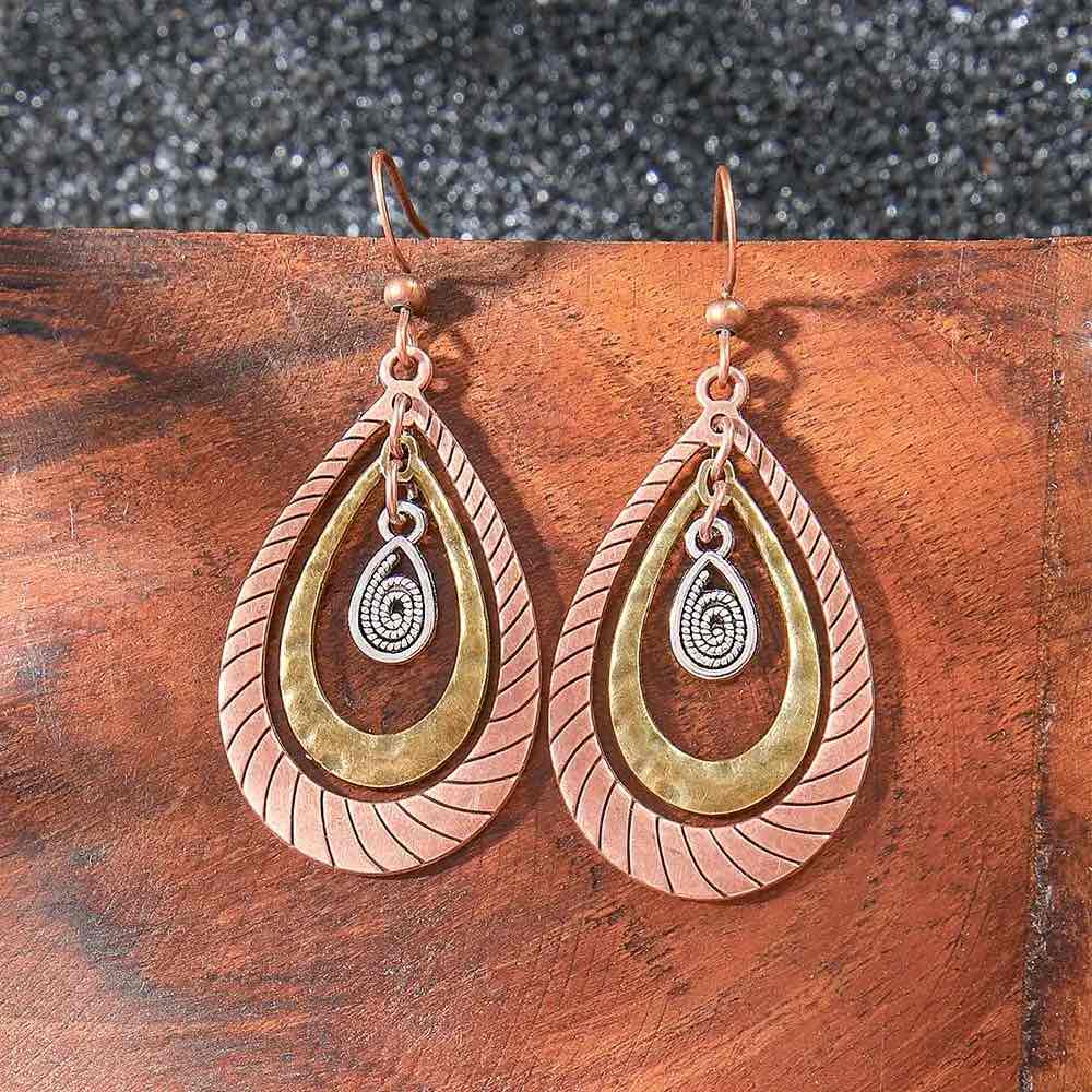 Oxidised earrings with a unique layered teardrop design in copper, antique gold, and silver, shown on a rustic wooden background.