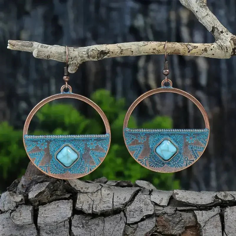 A pair of oxidised earrings with a half-hoop design and a turquoise stone, hanging from a tree branch.