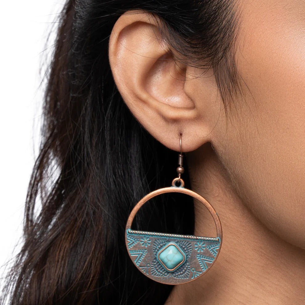 A woman wearing a single oxidised earring with a half-hoop design and a turquoise stone, showcasing the dangle style.