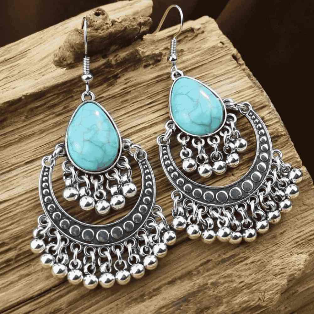 Close-up of a pair of oxidised silver drop earrings with teardrop turquoise stones, displayed on a rustic wooden surface.