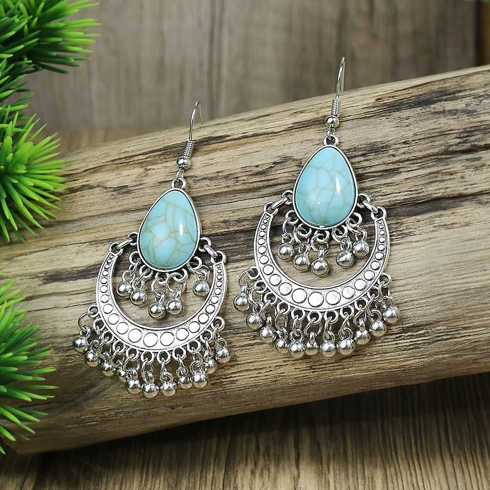 A pair of oxidised silver drop earrings with teardrop turquoise stones, resting on a wooden surface with green foliage in the background.