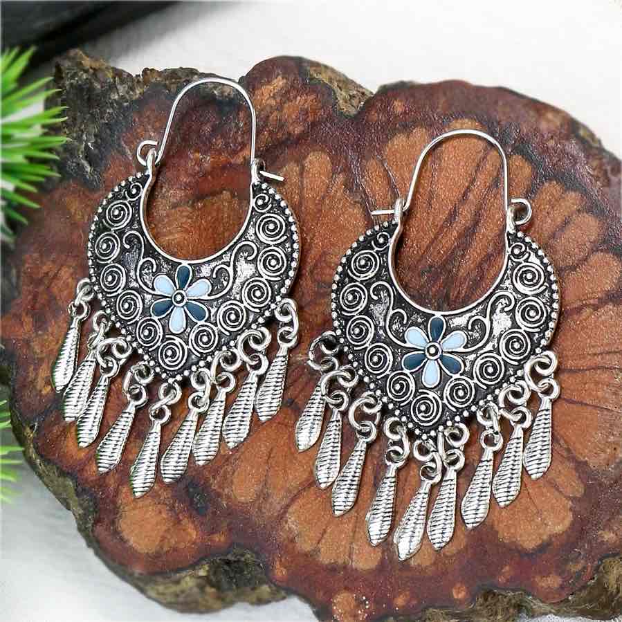 A pair of oxidised earrings with a crescent shape, blue floral detail, and multiple dangling elements, displayed on a wooden surface.