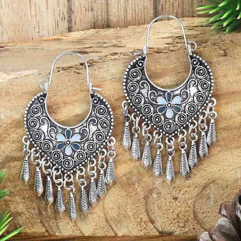 Two oxidised silver earrings, one slightly larger, with blue floral accents and dangling silver beads, presented on a rustic wooden background.
