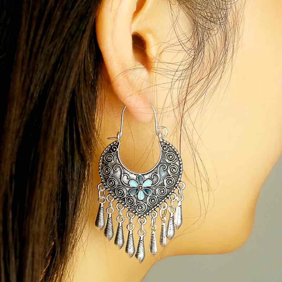 A model wearing a single oxidised earring, showcasing its crescent design, blue flower, and dangling silver elements against her ear.