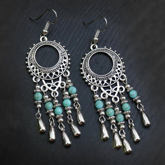 A pair of oxidised earrings featuring a circular filigree design with turquoise bead drops, displayed on a dark background.