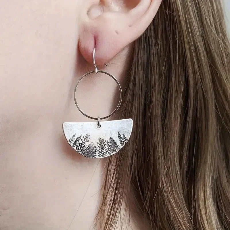 A close-up of a woman wearing an oxidised earring with a half-moon forest fern design.