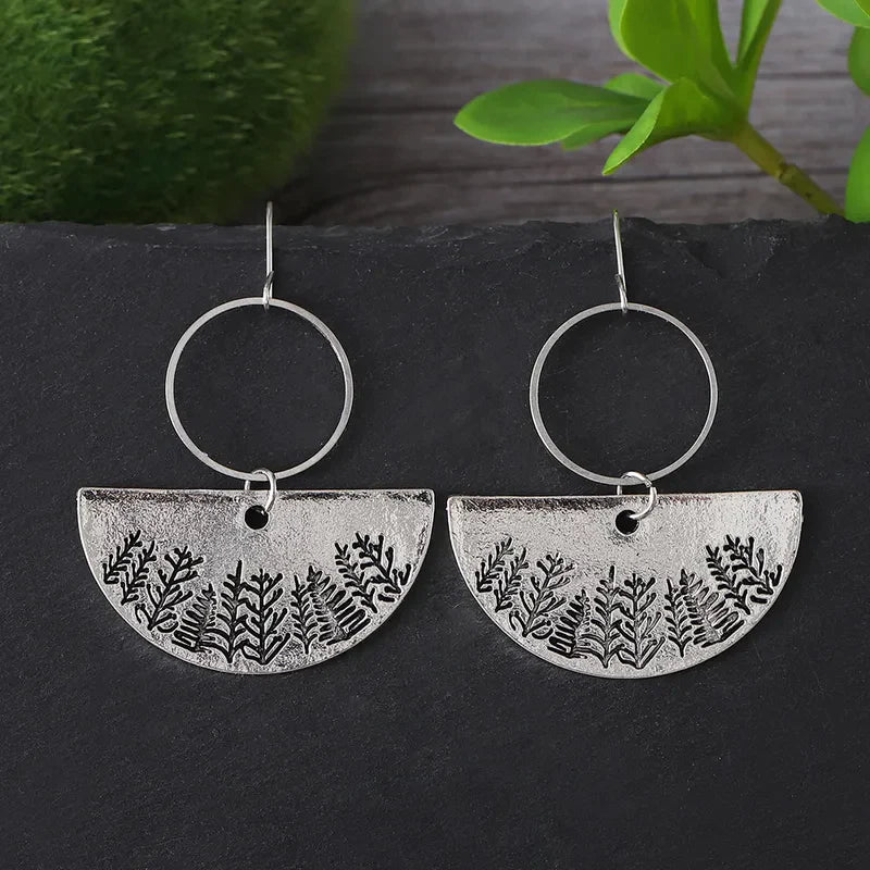 A pair of oxidised earrings with a half-moon forest fern design displayed on a dark surface.
