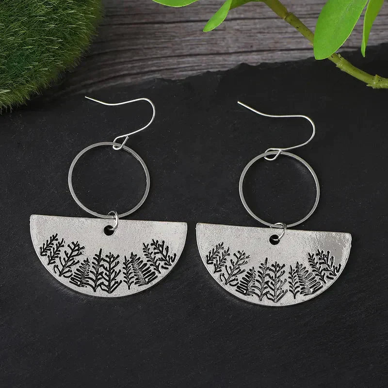 A close-up of one oxidised earring with a half-moon forest fern design.