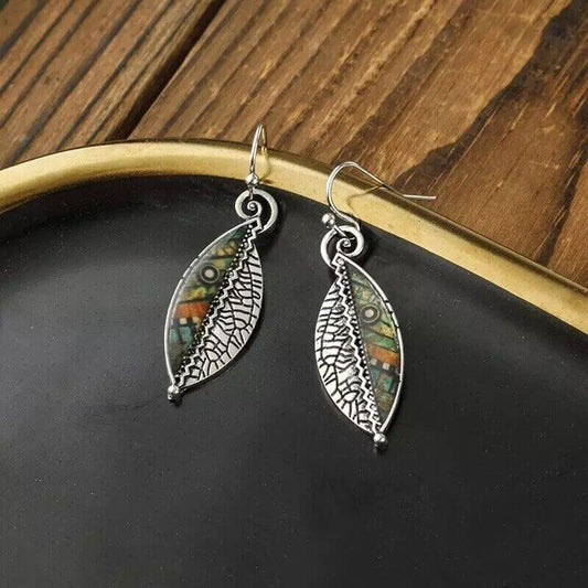 A pair of oxidised earrings with a leaf dangle design, featuring mosaic and filigree art, displayed on a black and gold tray.
