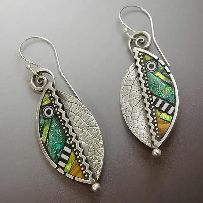 Close-up of oxidised earrings with a leaf shape, showcasing vibrant mosaic patterns in green, yellow, and orange, alongside textured silver filigree.