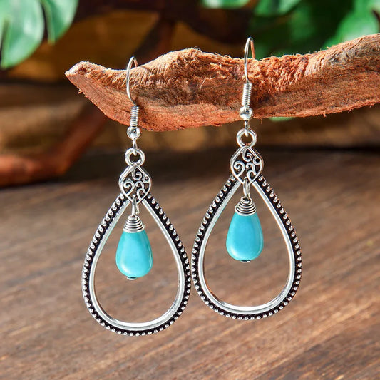 A pair of oxidised silver teardrop boho earrings with turquoise beads hanging from a wooden branch, showcasing their bohemian style.