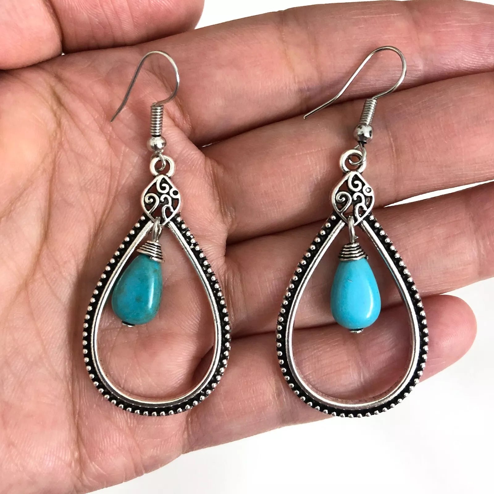 A hand holding a pair of oxidised silver teardrop boho earrings with turquoise beads, highlighting the intricate filigree and geometric pattern.
