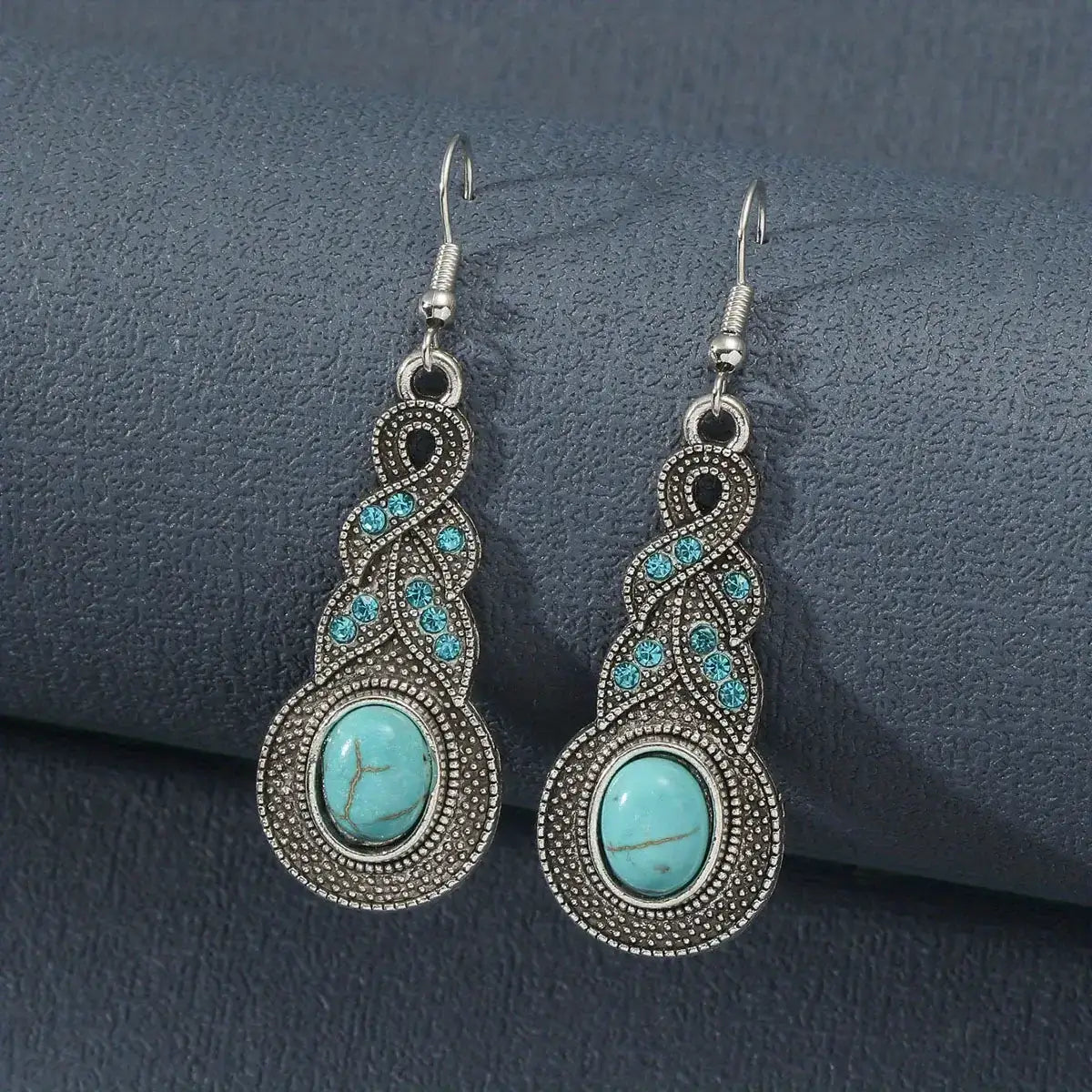 A pair of oxidised earrings featuring a prominent turquoise oval stone and delicate silver filigree, displayed against a dark grey background.