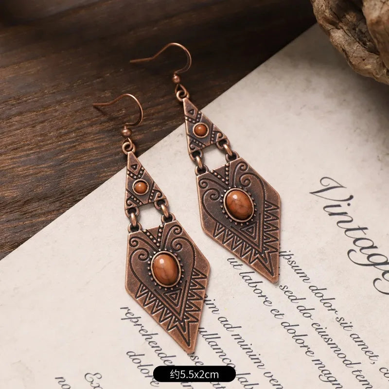 A pair of oxidised tribal stone drop earrings with bohemian dangle design, featuring brown stones and etched patterns, placed on a vintage-style paper with text.