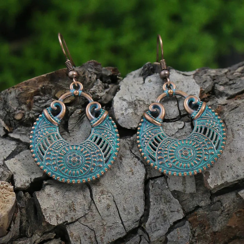 A pair of oxidised turquoise earrings with an ornate crescent design, hanging on a wooden surface.