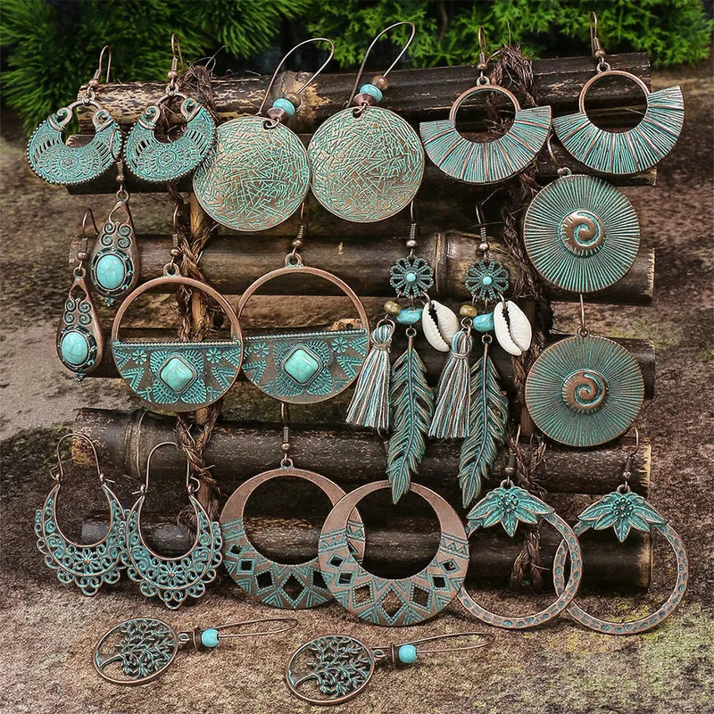 A collection of various oxidised earrings in turquoise and copper tones, including bohemian and dangle styles, displayed on wooden logs.