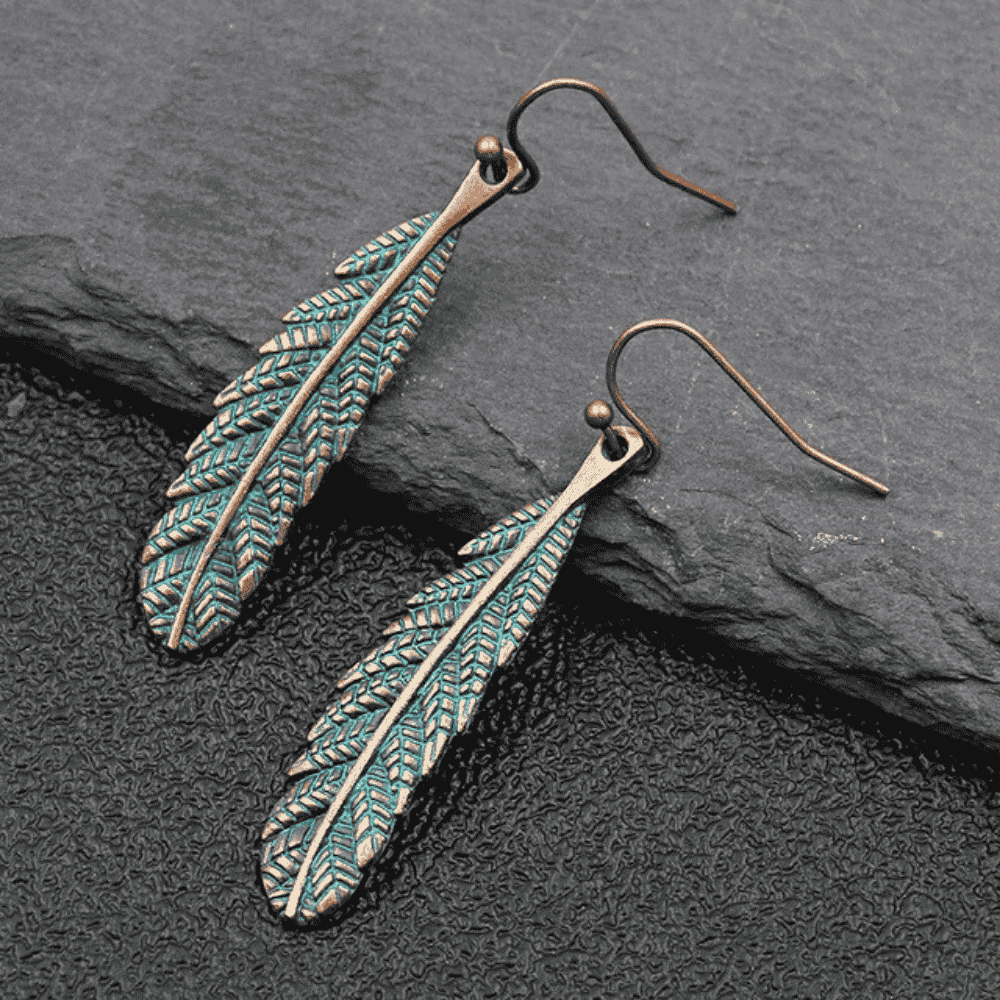 Unique oxidised feather dangle earrings with antique teal patina on dark background - front view | Earthy Origin