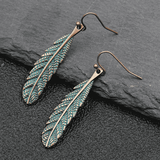 Unique oxidised feather dangle earrings with antique teal patina on dark background - front view | Earthy Origin
