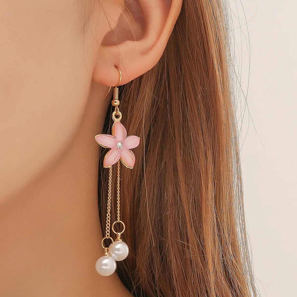 Close-up of a woman wearing a pink floral drop earring with pearl chains, showcasing the design.