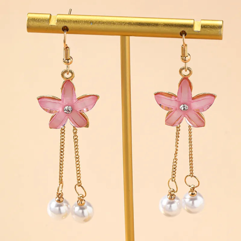 A pair of pink floral drop earrings with pearl chains displayed on a gold earring stand, highlighting both earrings.